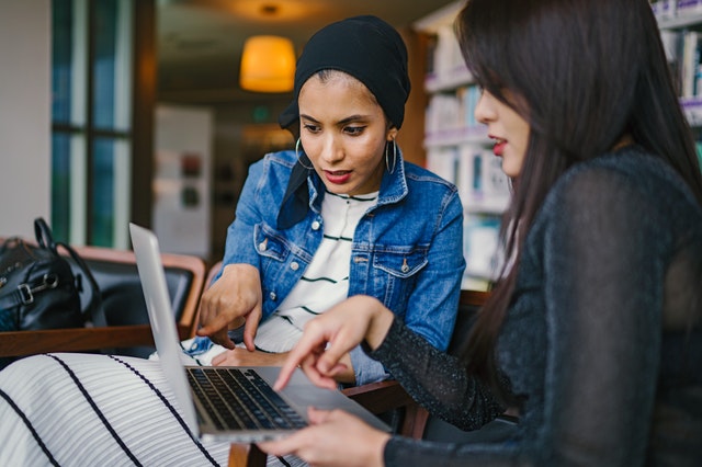 Dos mujeres de una agencia digital de servicio completo apuntando a una computadora portátil discutiendo estrategias.
