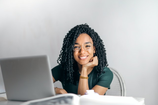 Una mujer de una agencia digital de servicio completo con la mano en la barbilla sonriendo mientras escribe en una computadora portátil.